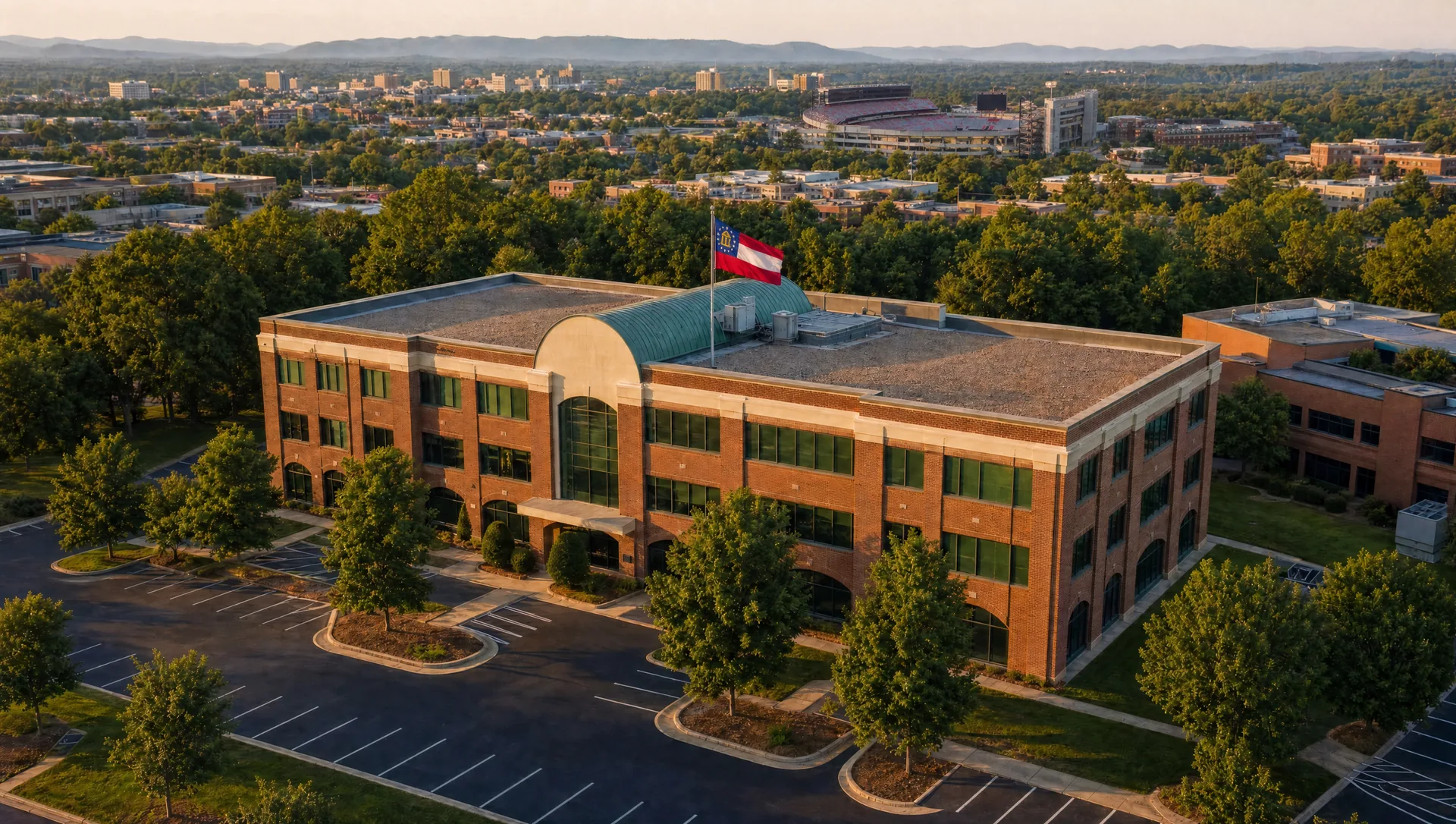 Aerial view at golden hour of the Nichols Land office building in Athens, Georgia, with the Georgia state flag flying and the Athens skyline and Sanford Stadium in the distance